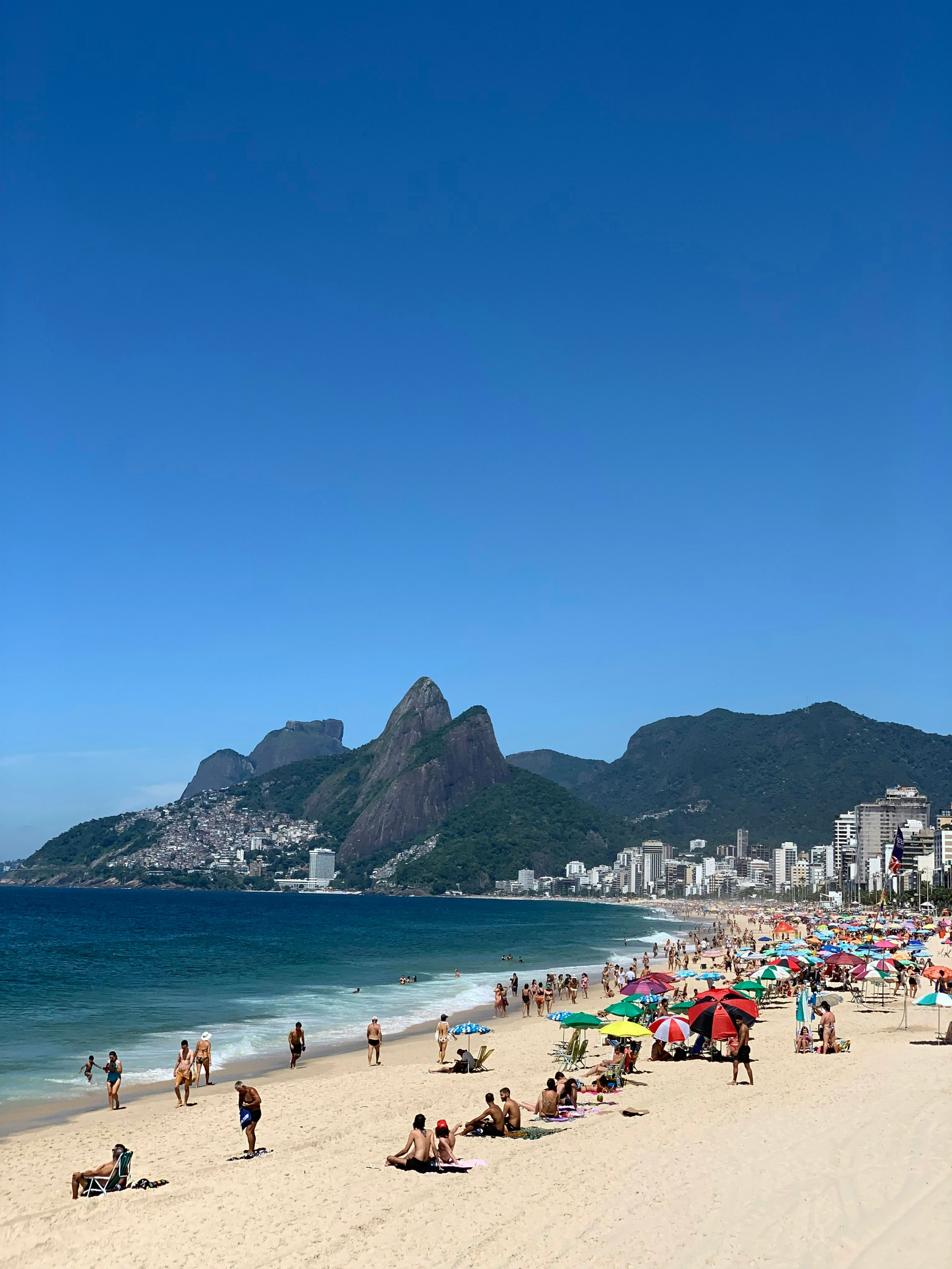 Colorful umbrellas and beachgoers beneath the Dois Irmãos peaks at Ipanema
