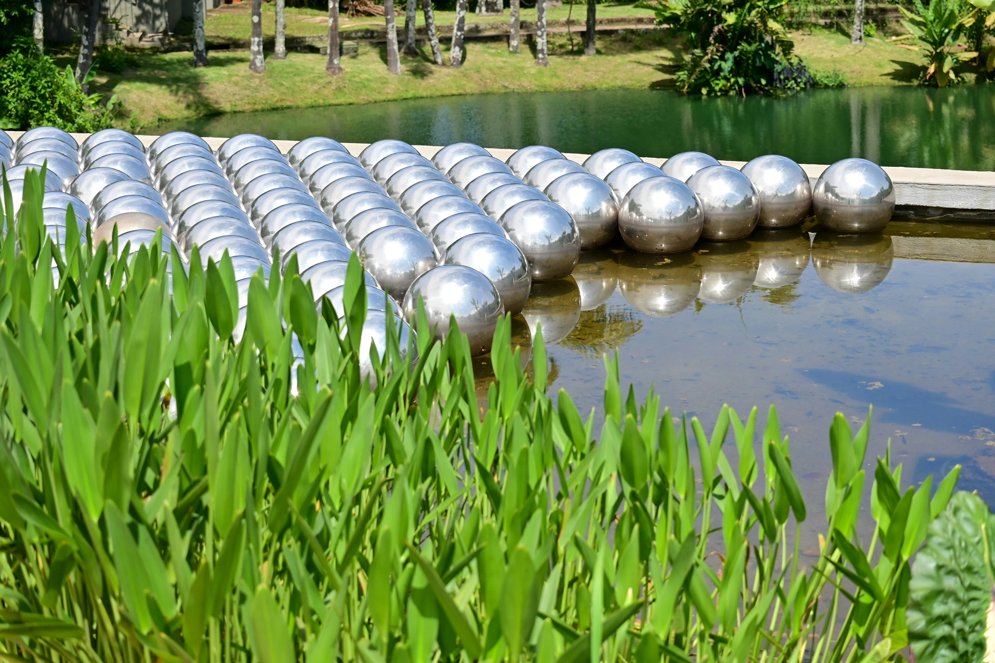 Mirrored spheres of Narcissus Garden reflect the landscape beside water at Inhotim