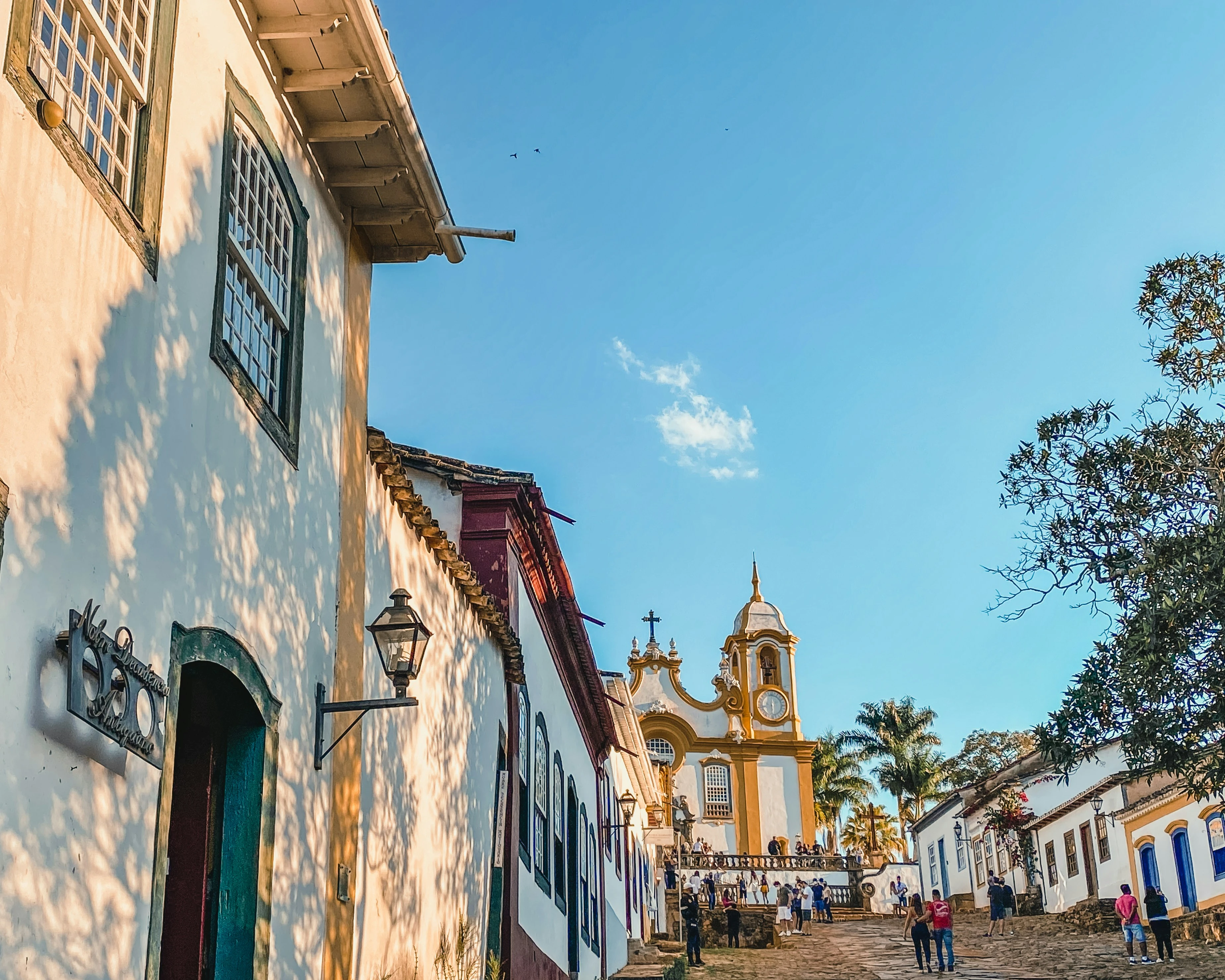 People walk toward Santo Antônio church along Tiradentes' sunlit stone street