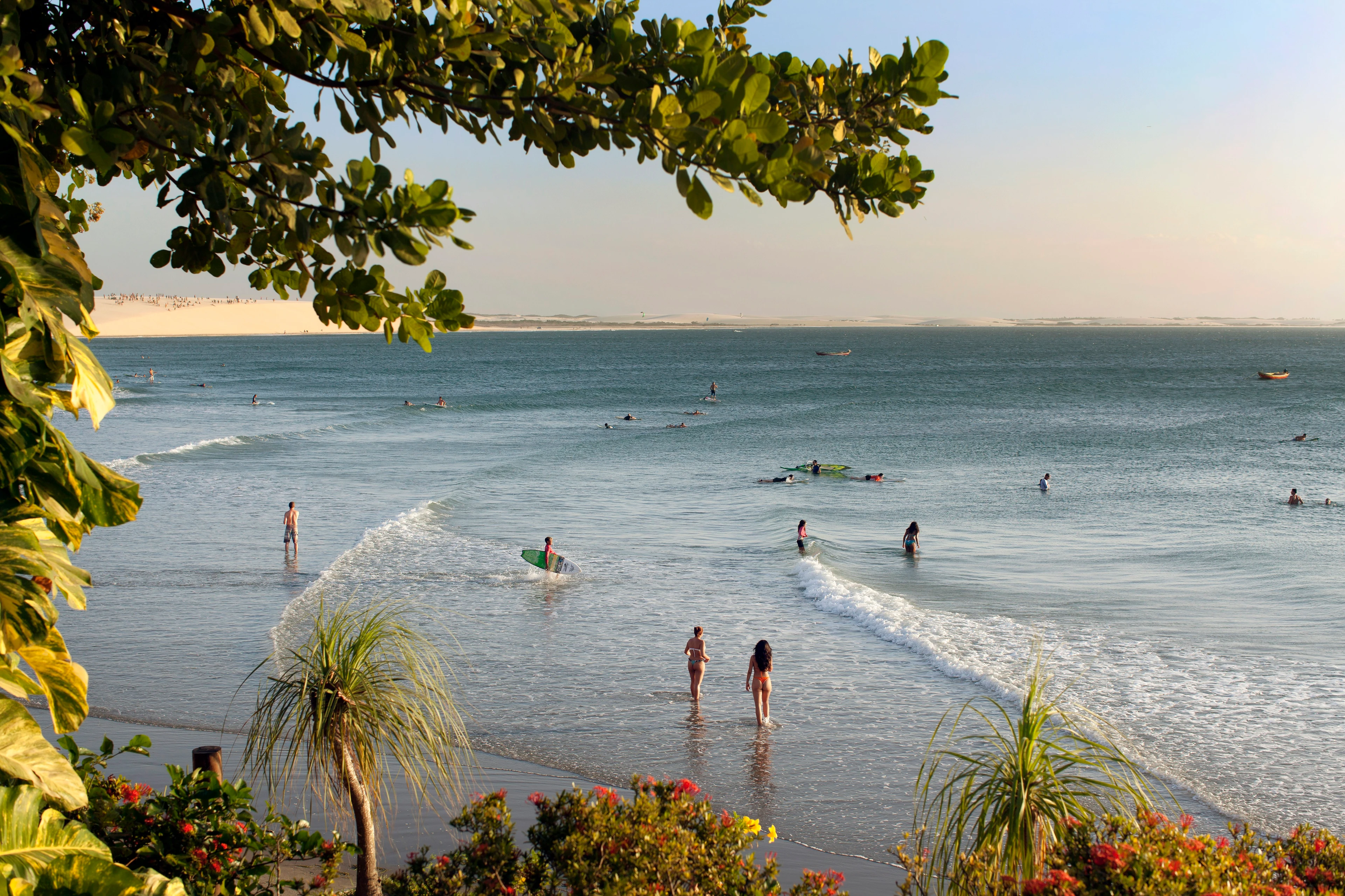 Sunlit waves, beachgoers and palms along the Jericoacoara coast